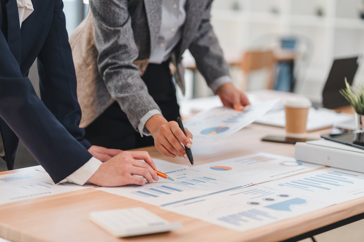 Two business professionals analyzing financial charts and graphs on a wooden desk in a modern office setting