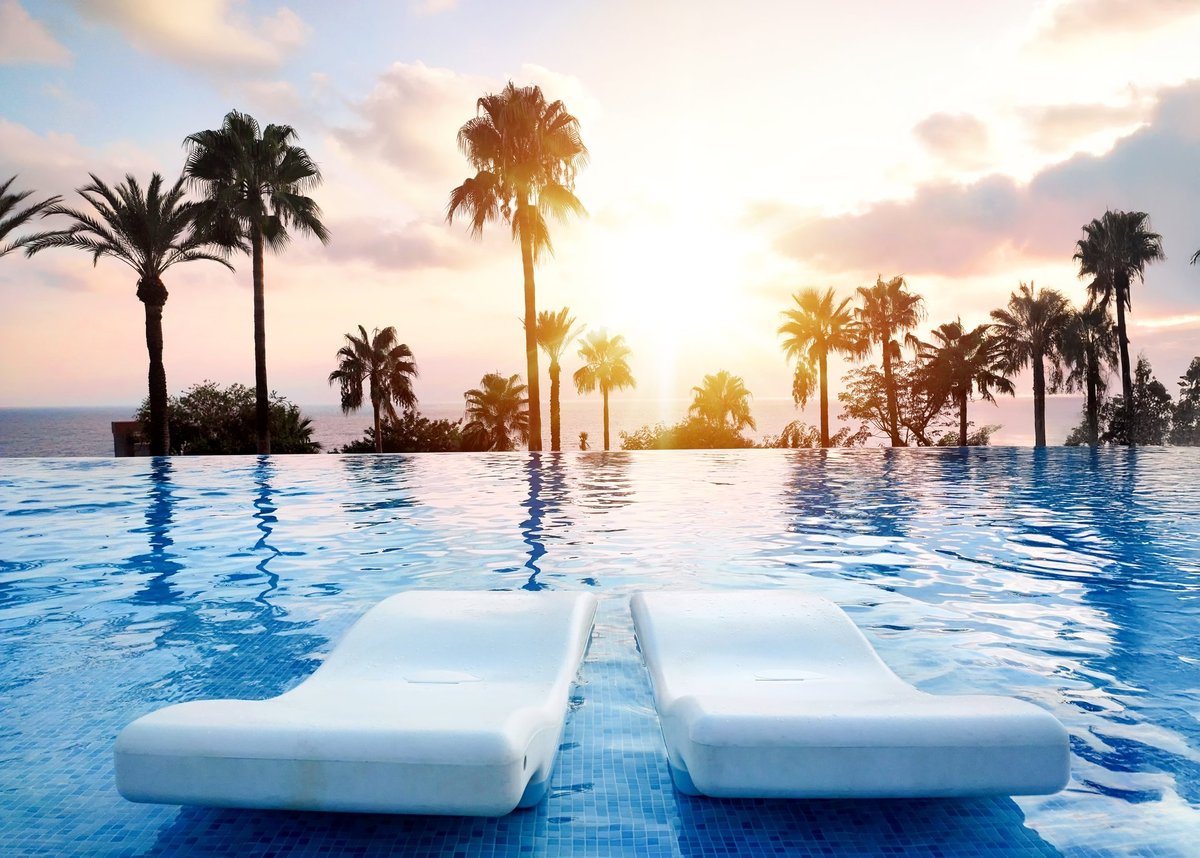 A tranquil sunset view over an infinity pool with palm trees, ideal for relaxation and vacation tropical themes