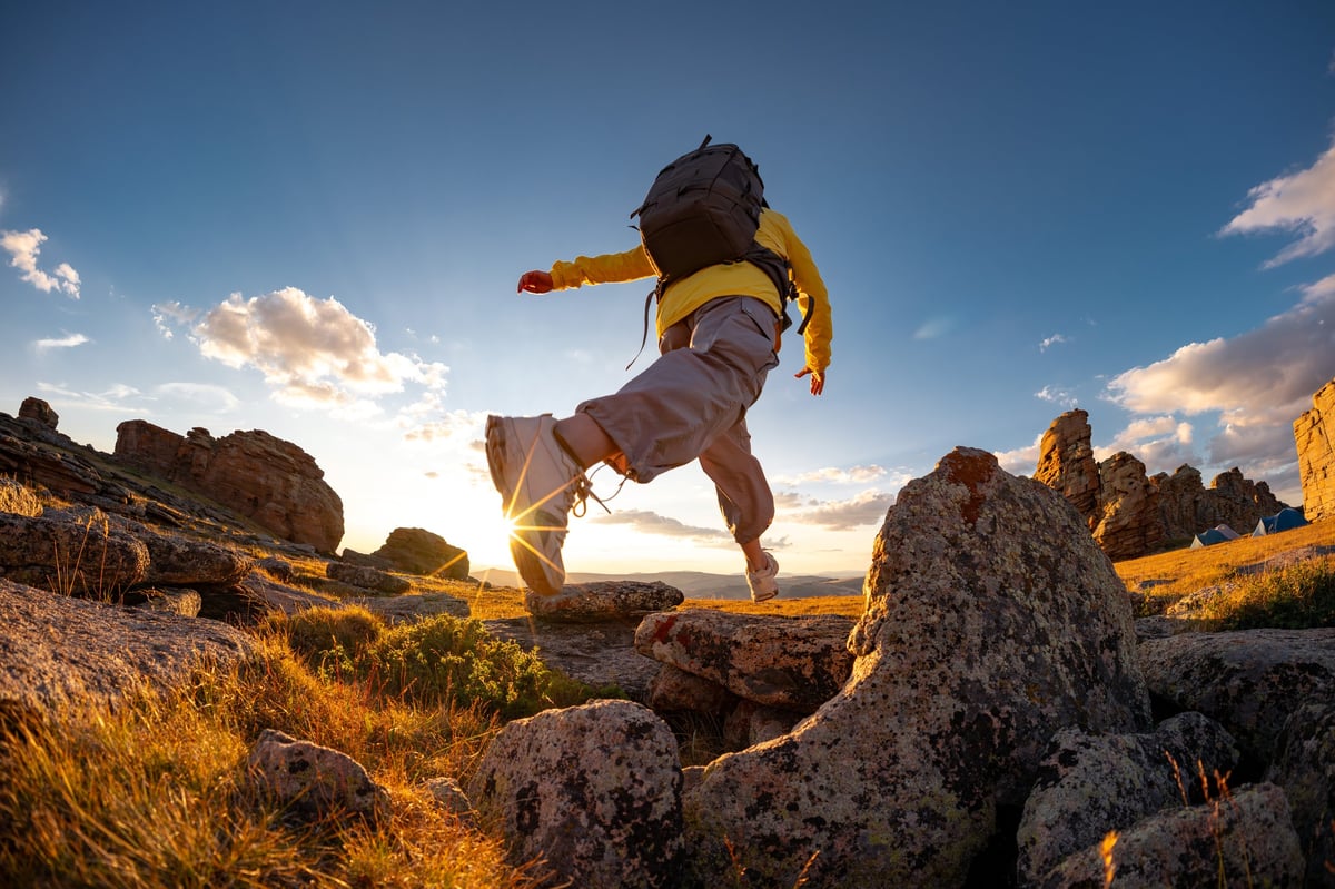 Wanderin springt über Felsen bei Sonnenuntergang