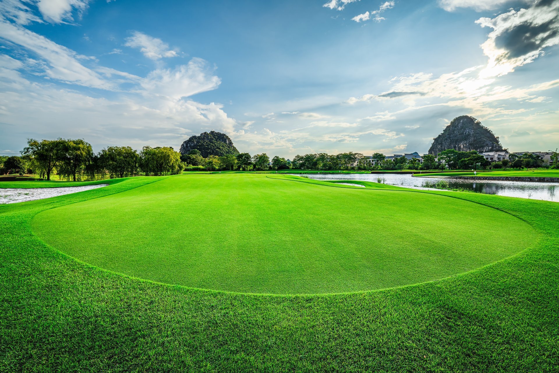 Manicured golf greens beside water and mountains