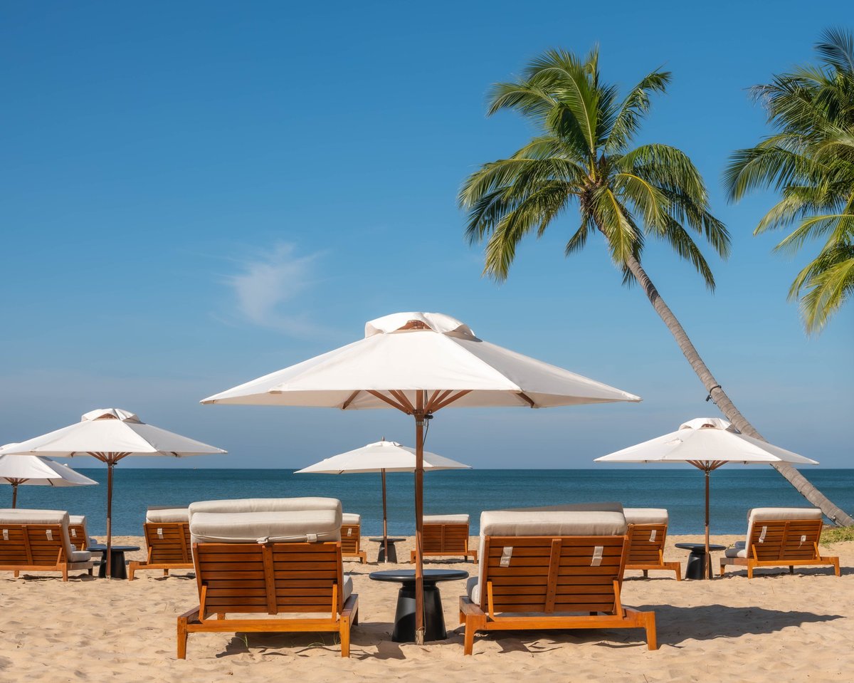 A serene, sunny view of a tropical beach featuring wooden lounge chairs and white umbrellas, perfect for a relaxing vacation getaway.
