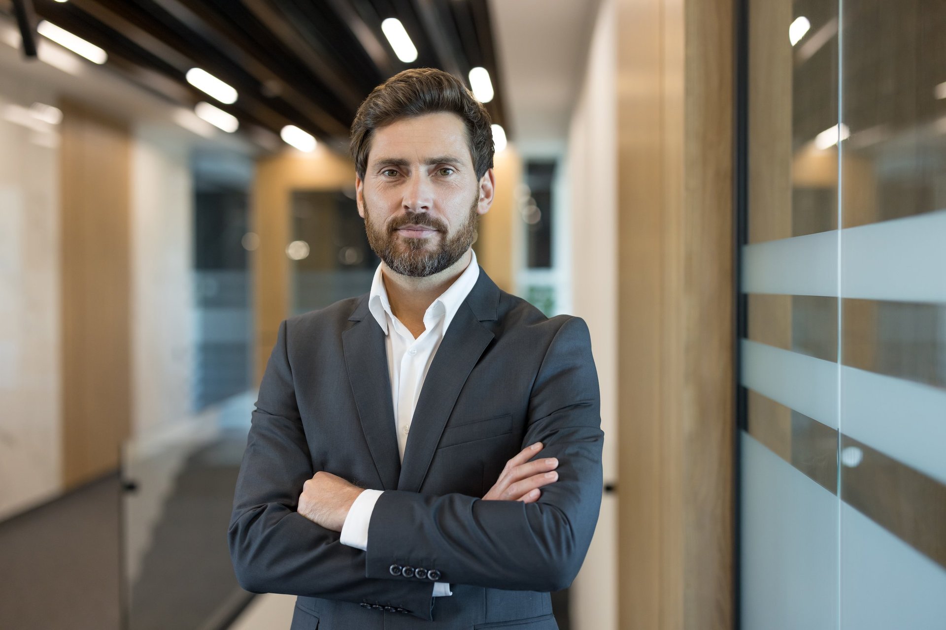 Confident businessman standing with arms crossed in a professional corporate office, portraying leadership and ambition