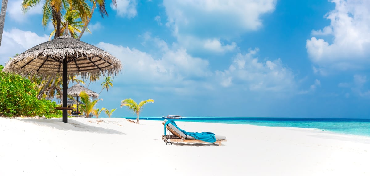 Sunny tropical Caribbean paradise resort beach with white sand, lounger and palms in the Maldives