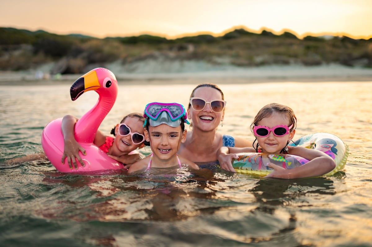 Family with three children swimming and playing in the ocean at sunset